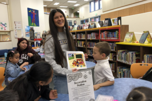 A teacher holding a piece of paper with children and college students at a table